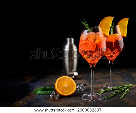 Wineglass of ice cold Aperol spritz cocktail served in a wine glass, decorated with slices of orange and rosemary branch. Black background. Copy space Royalty-Free Stock Photo #2000032637