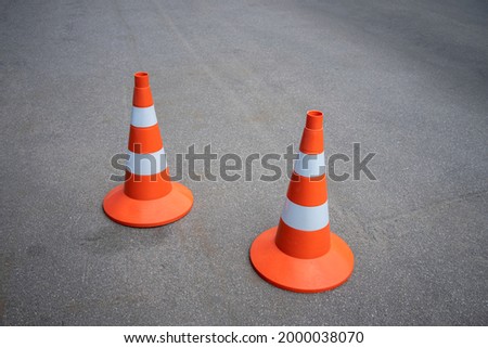 Two orange construction cones with reflective stripes on an asphalt road, repair of the roadbed on the motorway