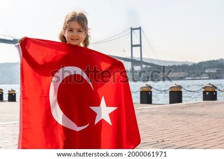 Girl hold Turkish flag near Bosphorus bridge (aka15 July Martyrs Bridge or 15 Temmuz Sehitler Koprusu) in Ortakoy, Istanbul, Turkey. Patriotism. Turkish National Sovereignty and and Children's day.
