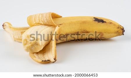 A peeled and bitten banana in a peel on a white background. Old one peeled banana. Tropical yellow fruit. Selective focus. Bitten Banana. Royalty-Free Stock Photo #2000066453