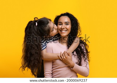Mothers Day Concept. Adorable Little Girl Embracing And Kissing Her Arab Mom, Portrait Of Happy Middle Eastern Mother And Daughter Bonding Together Over Yellow Studio Background, Copy Space