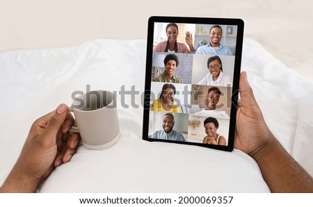 Black male videochatting with group of friends while relaxing with digital tablet and coffee in bed, young African American man and woman having web conference together, creative collage, cropped