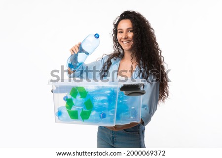 Smiling Female Putting Plastic Bottle To Box With Recycling Symbol Sorting Waste Smiling To Camera Standing Over White Background In Studio. Recycle Junk Disposal Concept
