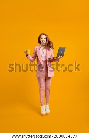 Full length profile photo of funny business lady jump high up hold laptop and cup of coffee in hands addicted worker always online wear pink suit outfit, white sneakers, isolated yellow background