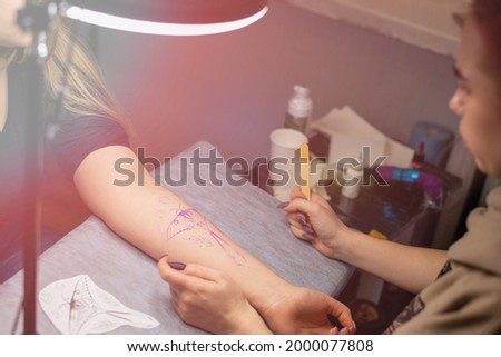Close up temporary tattoo on arm of client which making worker. Preparation. Transfer the sketch to the body.