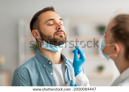 Nasal coronavirus PCR test. Doctor using swab stick to take covid virus specimen from potentially infected young guy at home. Viral disease prevention and diagnostics concept Royalty-Free Stock Photo #2000084447