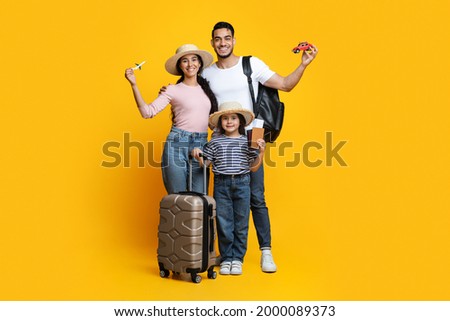 Portrait Of Happy Arab Family With Little Daughter Ready For Vacation, Cheerful Middle Eastern Parents And Their Child Standing With Suitcases, Pasports And Travel Souvenirs Over Yellow Background
