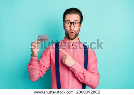 Photo of impressed cute young guy dressed pink shirt spectacles pointing finger credit card isolated turquoise color background