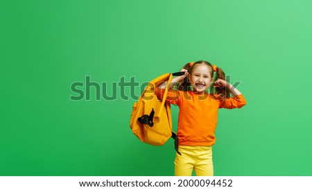 Back to school. happy little schoolgirl with two ponytails, in fashionable clothes and with backpack shows off her muscles. confident, strong and successful girl smiles and poses on green background.