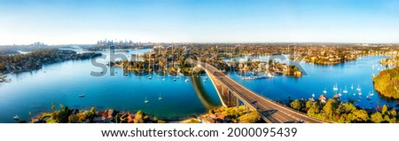 Modern Gladesville bridge over Parramatta river to Drummoyne in view of distant Sydney city CBD skyline - aerial panorama. Royalty-Free Stock Photo #2000095439