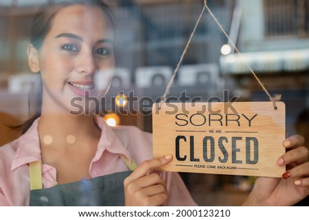 Smiling asian young owner retail, coffee shop woman turning sign board to closed after finished work, job and protection to pandemic of coronavirus. Close store due to lockdown, quarantine of covid.