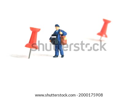 Miniature people toys conceptual photography. Courier pinpoint location pickup package delivery service. Postman with red push pin, isolated white background.