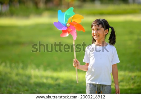 Cute little girl playing on the colorful toy windmill  in her hands at the lawn. Which increases the development and enhances learning skills renewable energies and sustainable resources.