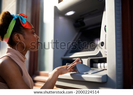 Beautiful african women using ATM machine. Attractive young woman withdrawing money from credit card at ATM.	

