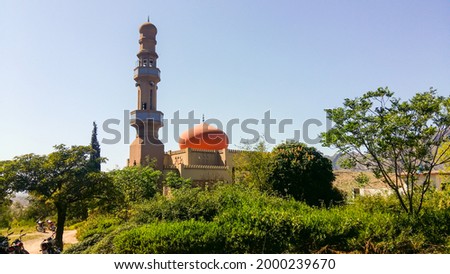 A view of a historical graceful mosque with colored dome and a long minaret surrounded by green trees in the daytime