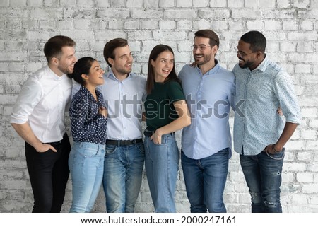 Happy diverse interns or newcomer employees celebrating getting hired, sharing success, hugging, talking, laughing. Smiling people discussing together teamwork. We are like multi racial family Royalty-Free Stock Photo #2000247161