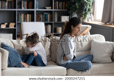 Angry Caucasian mother and small daughter sit separate back to back after family fight or quarrel. Mad unhappy mom and little kid child avoid talking, have misunderstanding. Generation gap concept. Royalty-Free Stock Photo #2000247251