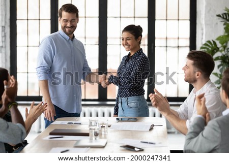 Happy Indian female team leader shaking hands with proud employee, thanking promoted worker for good job and congratulating with reward. Millennial business group welcoming newcomer with applause Royalty-Free Stock Photo #2000247341