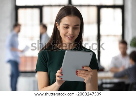 Happy female manager using tablet computer for video call, giving consultation to client. Young intern or student holding electronic gadget in office, studying educational app on pad, reading guidance Royalty-Free Stock Photo #2000247509