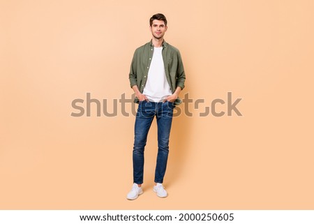 Photo of charming confident young guy dressed green shirt smiling walking arms pockets isolated beige color background Royalty-Free Stock Photo #2000250605