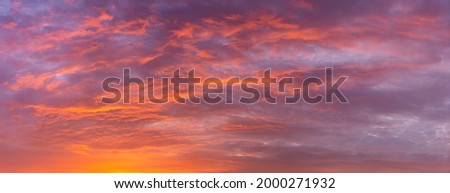 Vibrant dramatic panorama of cloud blanket texture and detail brightly colorful lit up orange from below at sunset with blue tints in the background. Painterly weather condition wallpaper backdrop. Royalty-Free Stock Photo #2000271932