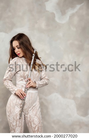 Portrait young woman model in stage costume dress with flute in hands. Wind instrument at flute player on background of textured wall. Poster for advertising school. Concept piece of music or concert