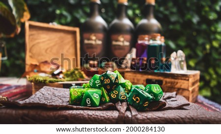 Image of a pile of green RPG gaming dice on top of a leather-bound book. Within the background wooden boxes with bottles containing a various colored liquid