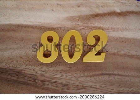 Gold Arabic numerals 802 on a dark brown to off-white wood pattern background.