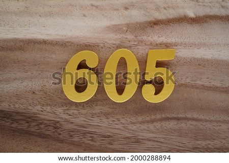 Gold Arabic numerals 605 on a dark brown to off-white wood pattern background.