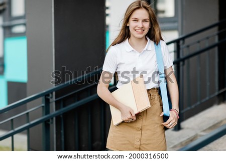 Portrait of a smiling female student with a book and backpack on the way to college