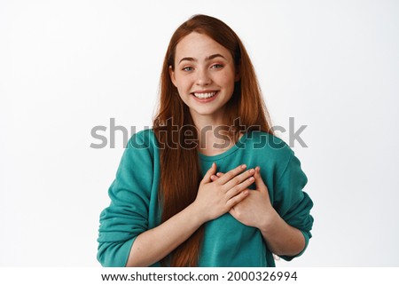 Always in my heart. Smiling young woman with red hair, feeling touched and grateful, say thank you, feeling heartfelt, standing against white background Royalty-Free Stock Photo #2000326994