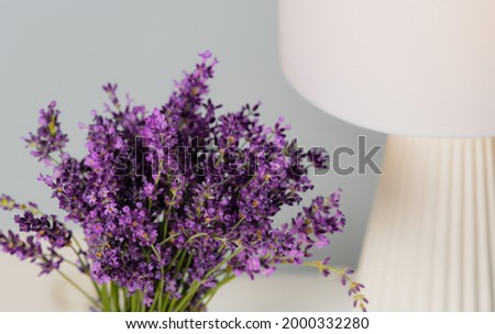 Floral deco photography. A beautiful bouquet of purple lavender flowers in a glass vase next to a lamp. Interior design idea.