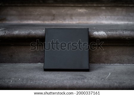 Square empty black canvas stands on stone steps. Mockup canvas (931)