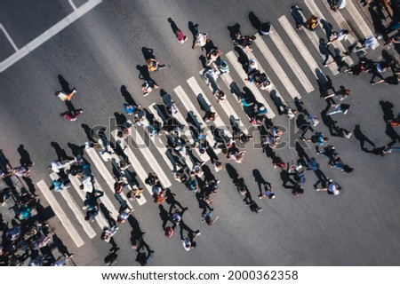 Different blurred people at a pedestrian crossing in the city - drone shot. People at a zebra pedestrian crossing - a lot of pedestrians in an overcrowded city on a sunny day. Aerial drone shot. 