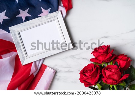 Concept of U.S. Independence day or Memorial day. National flag and red rose over bright marble table background with picture frame.
