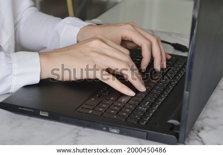 Close up photo of female office employee hands typing on black laptop.