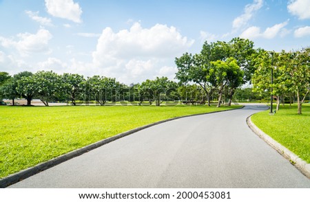 Beautiful green city park with blue sky. Pathway and beautiful trees track for running or walking and cycling relax in the park on green grass field on the side. Sunlight and flare background concept. Royalty-Free Stock Photo #2000453081