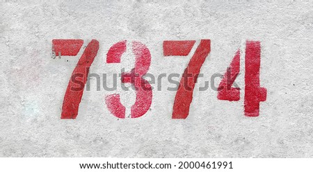 Red Number 7374 on the white wall. Spray paint. Number seven thousand three hundred and seventy four.