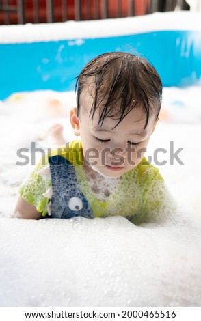 Little Asian boy enjoys swimming and playing with bubbles in an inflatable pool. summer water play, family happiness, children's happiness. vertical picture