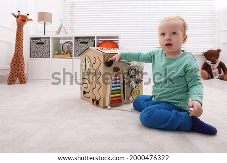 Cute little boy playing with busy board house on floor at home