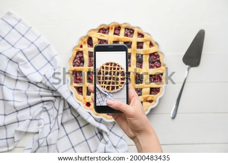 Female food photographer with mobile phone taking picture of tasty cranberry pie, top view