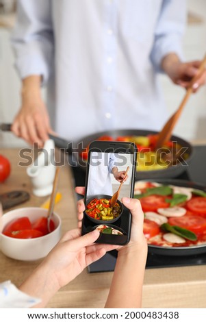 Little girl with mobile phone taking photo of female chef in kitchen
