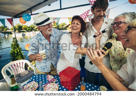 Senior people celebrating birthday in the cottage on the river singing karaoke.