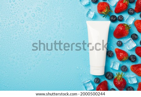 Above photo of berries strawberries blueberries transparent cubes ice water drops and white tube of cream isolated on the blue background with copyspace Royalty-Free Stock Photo #2000500244
