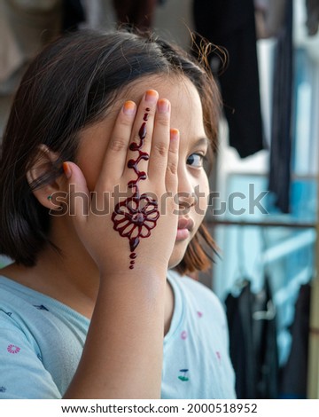 Portrait of Henna ornaments on young girl's hand covering face.