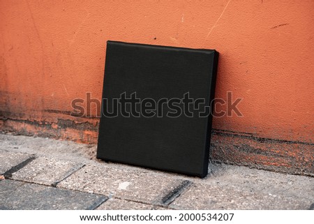Black square blank printable canvas stands near a red stone wall. Canvas mockup (939)