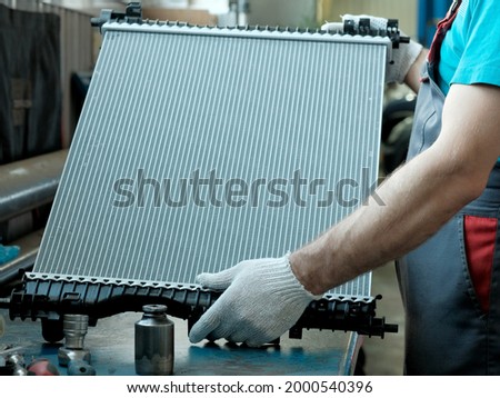 Spare parts for a passenger car.Radiator of the cooling system in close-up. An auto mechanic holds a new radiator in his hands.Repair and maintenance of the car in the service center. Royalty-Free Stock Photo #2000540396