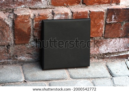 Black empty square printable canvas near a brick red wall. Mockup canvas (942)