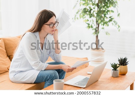 Busy thoughtful pensive serious young businesswoman freelancer student e-learning doing paperwork at home office, paying bills, checking documents and contracts, mortgage and e-banking concept Royalty-Free Stock Photo #2000557832