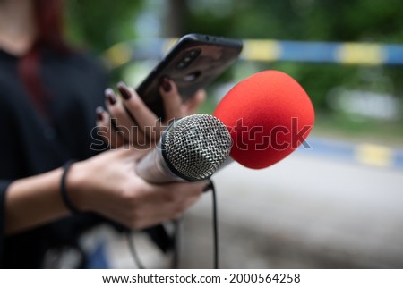 Female journalist at news conference, recording notes, holding microphone and smarthopne lice dictaphone